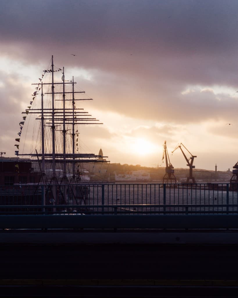 Göteborgs hamn vid solnedgång — segelfartyg och silhuett av staden.